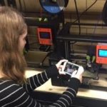 Picture of student working in the Innovation and Collaboration Studio, using her phone to take a picture of a 3D printer