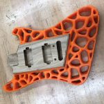 Picture of a guitar body made in the Innovation and Collaboration Studio; body made with 3D printed orange plastic around a wooden core