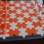 Picture of a 3D printed chess board, with orange and white squares shaped like puzzle pieces
