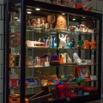 Picture of a lighted display case in the Innovation and Collaboration Studio; its shelves are filled with various 3D printed objects